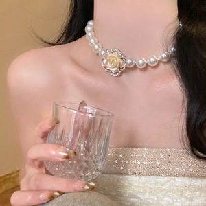 Close-up of a layered pearl necklace with a diamond-encrusted camellia flower on a model