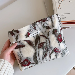 Macro detail of vintage floral embroidery and simple wish label on beige fabric pouch