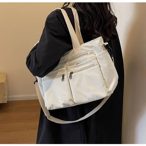 Detail of off-white corduroy tote bag showing front zipper pockets and shoulder strap