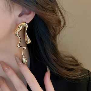 Macro close-up of irregular liquid gold earrings worn by model for elegant style