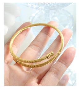 Detail shot of a minimalist gold twisted rope open bangle with unique bead decoration