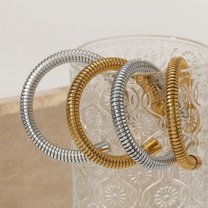 Artistic display of gold and silver flexible snake chain bracelets on a glass rim