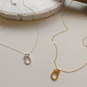Close-up of minimalist gold and silver knot pendant necklaces on white stone base