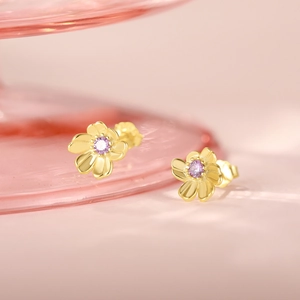 Macro shot of gold floral earrings with pink crystal center on a soft pink background