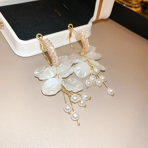 Detail of gold petal earrings with pearls and cubic zirconia on a white jewelry box