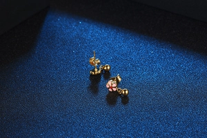 Detail view of pink flower stud earrings with golden metal ball pendants and butterfly backs