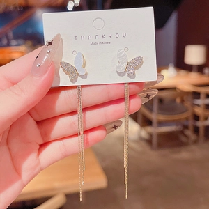 Detailed close-up of a gold butterfly earring with shell wings and long tassel chains