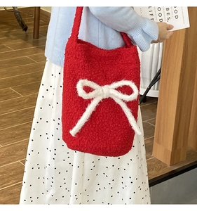 Detail of red plush bucket bag featuring a large white knitted bow on fuzzy texture