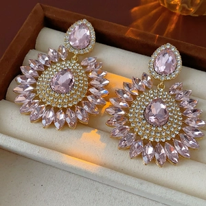 Detailed macro of gold drop earrings with pink crystals on a jewelry box cushion