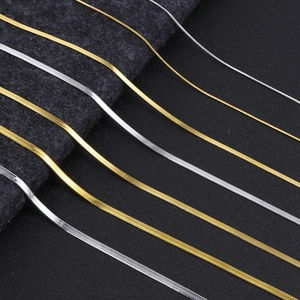 Detail showing various sizes of gold and silver snake chains on textured fabric