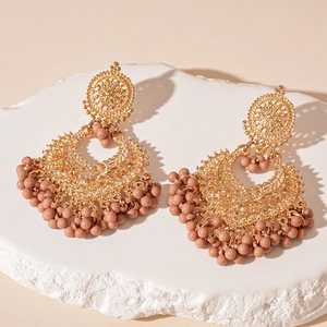 Detail of bohemian gold hollow earrings with dusty pink bead tassels on a stone base