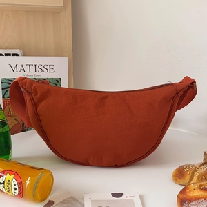 Orange crescent nylon crossbody bag with adjustable strap in casual lifestyle setting