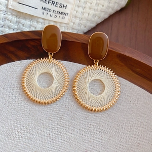 Detailed view of bohemian woven hoop earrings with brown resin tops on a textured linen background
