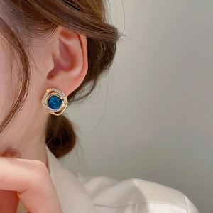 Close-up of a vintage square earring with blue gemstone and pavé diamonds on a model