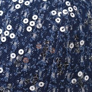 Detailed macro view of distressed denim fabric with silver sequins and frayed texture edges