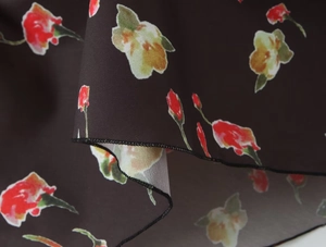 Nahaufnahme von geblümtem Chiffon mit roten und gelben Blumen und Nahtdetails am Saum