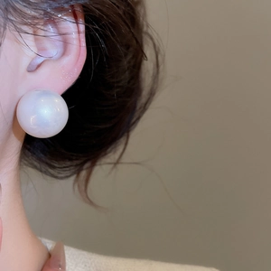 Close-up of a large round cream pearl earring with iridescent luster on a model's ear