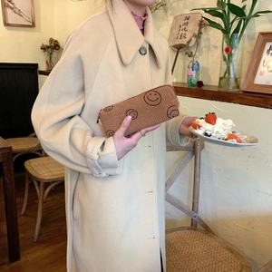 Detailed texture of brown corduroy cosmetic bag with embroidered smiles held by a model