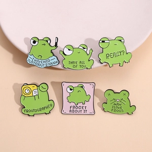Set of 6 cartoon frog enamel pins with funny slogans on a decorative pastel tray
