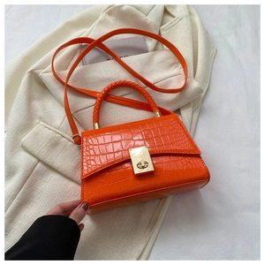 Detail of bright orange faux crocodile skin bag with golden metal twist lock and woven handle