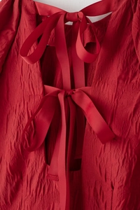 Détail du dos d'une robe rouge texturée avec plusieurs nœuds papillon et volants de tissu