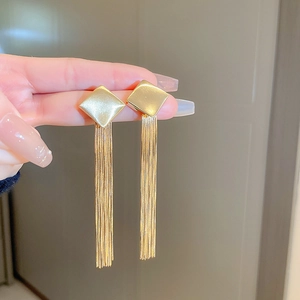 Close-up of golden geometric square earrings with elegant long tassel fringe on a model