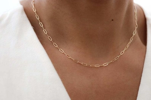 Gros plan d'un collier chaîne trombone doré porté par un mannequin en haut à col en V blanc