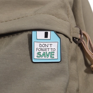 Dettaglio della spilla smaltata a forma di floppy disk blu su zaino in tela kaki