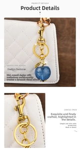 Detail of glittery dark blue apple keychain charm with gold leaves on a white leather bag