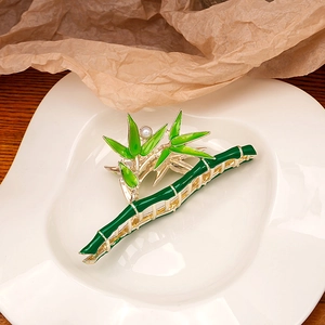 Detailed bamboo hair claw with green enamel leaves, golden metal texture, and pearl accents