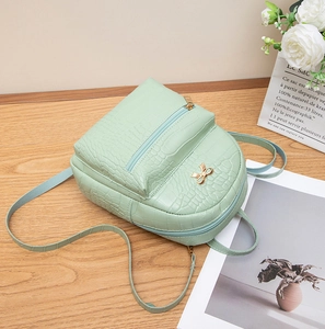 Mini light green backpack with crocodile pattern and golden bow detail on wooden desk