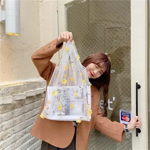 Close-up of white mesh tote bag featuring 3D yellow floral embroidery and dual handles
