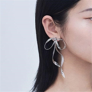 Macro side view of long silver ribbon bow earrings worn by model on a grey background
