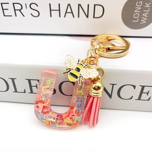 Detail of pink resin letter U keychain with gold bee charm and suede tassel accessory