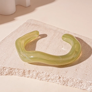 Detail of light green translucent acrylic bangle with irregular wavy texture on stone