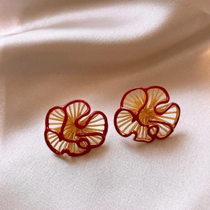 Macro shot of gold-plated petal earrings with red enamel edges on silk fabric