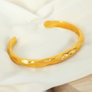 Minimalist irregular hammered gold open cuff bracelet on soft white fabric background