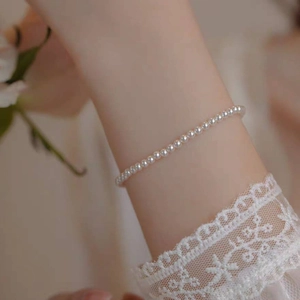 Close-up of minimalist 14k gold pearl bracelet on wrist with elegant white lace sleeve