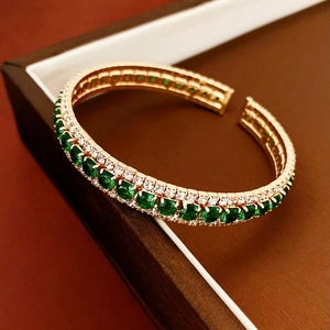 Detail of emerald cut green gemstone and white diamonds on a gold open cuff bracelet