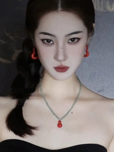 Close-up of a model wearing red gourd pendant necklace and heart-shaped enamel earrings