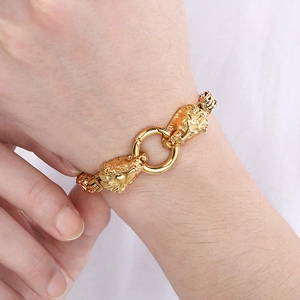 Dettaglio di due teste di leone dorate con anello su un bracciale da uomo in acciaio