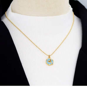 Detail of a gold ball chain necklace with a blue enamel round pendant and fish tail motif