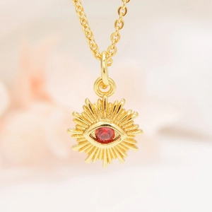 Detailed macro shot of a gold Evil Eye pendant featuring a central red zircon stone and micro-inlays