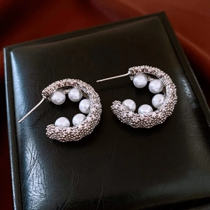 Macro view of C-shaped silver earrings with sparkling crystals and white pearls
