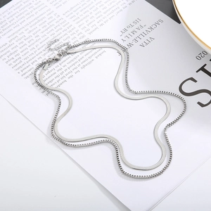 Close-up of double-layer silver minimalist blade and box chain necklace on artistic paper