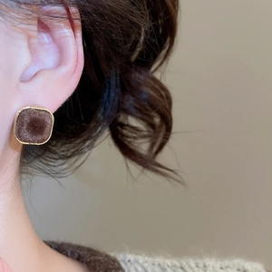 Detail of square flocked brown stud earrings with gold metal frame worn by a model