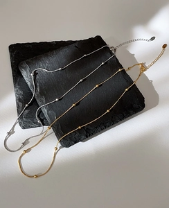 Macro detail of gold and silver snake chain necklaces with beads on a black stone tray
