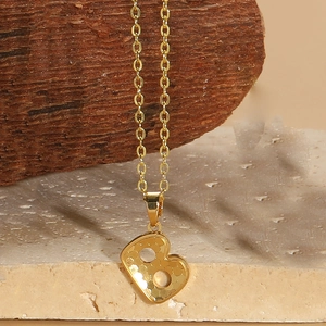 Macro shot of gold-plated necklace featuring a textured letter B pendant on stone base