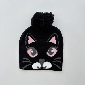 Detail of a kids black knit beanie with a large pom-pom and cute cat jacquard pattern
