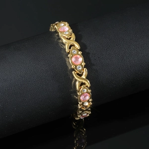 Detail of gold magnetic bracelet with pink gemstones and crystals on a black display stand